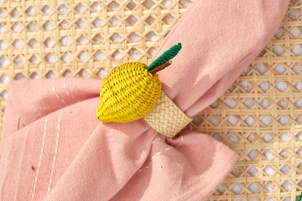 Yellow crocheted lemon-shaped napkin ring on a pink napkin with a woven background