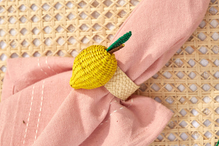 Yellow crocheted lemon-shaped napkin ring on a pink napkin with a woven background