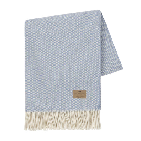 Light blue woven throw blanket with beige fringe and label on a white background