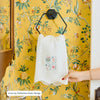 White apron with colorful icons held by a hand against a yellow floral-patterned wall.