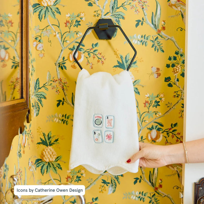 White apron with colorful icons held by a hand against a yellow floral-patterned wall.