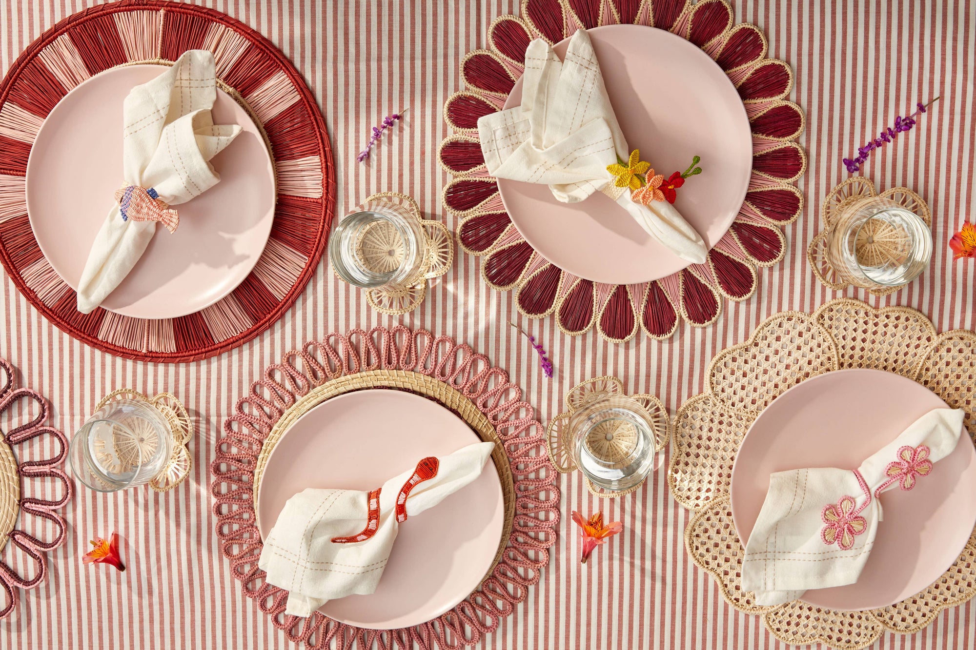 Decorative table setting with pink plates, red rimmed plates, and gold chargers on a striped tablecloth.