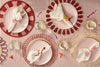Decorative table setting with pink plates, red rimmed plates, and gold chargers on a striped tablecloth.