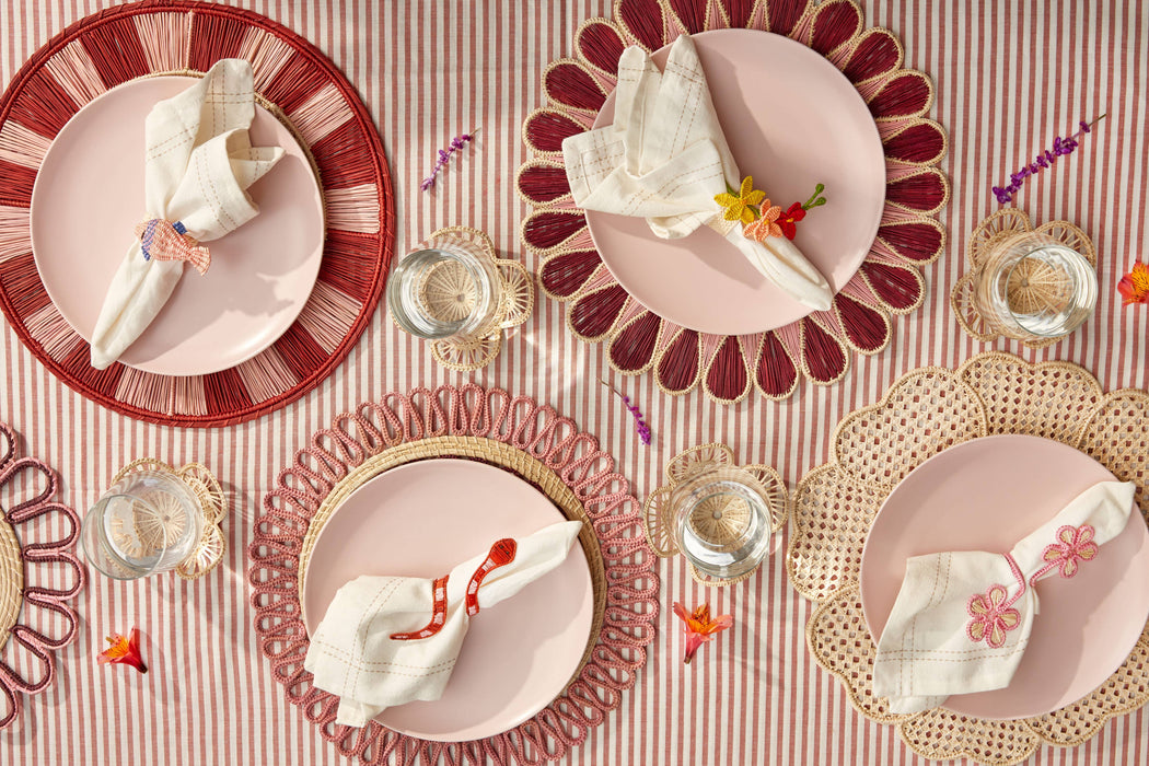 Decorative table setting with pink plates, red rimmed plates, and gold chargers on a striped tablecloth.