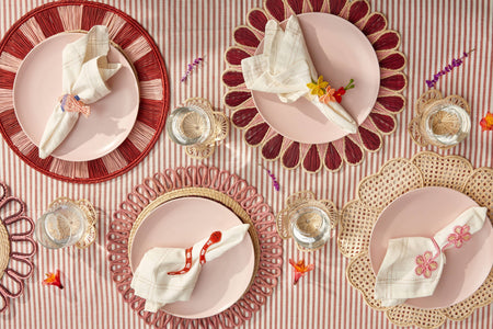 Decorative table setting with pink plates, red rimmed plates, and gold chargers on a striped tablecloth.