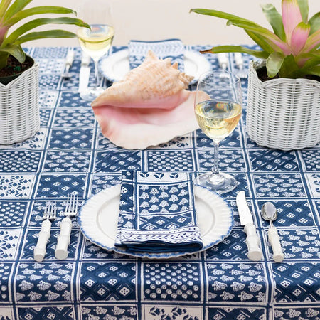 Table setting with blue and white patterned tablecloth, napkin, and glasses on a decorative table.
