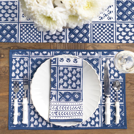 Blue and white patterned placemat with cutlery and a glass on a wooden table.