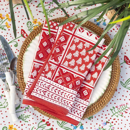 Red and white patterned napkins on a woven plate with a colorful tablecloth.