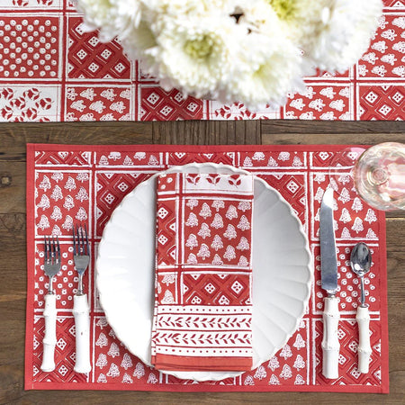 Red and white patterned placemat with cutlery on a wooden table.