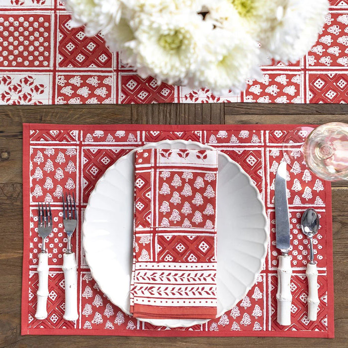 Red and white patterned placemat with cutlery on a wooden table.