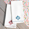 White towels with floral embroidery on a wooden surface with a floral patterned fabric in the background.