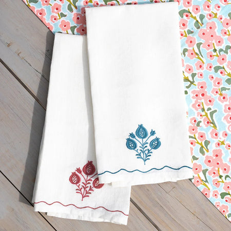 White towels with floral embroidery on a wooden surface with a floral patterned fabric in the background.