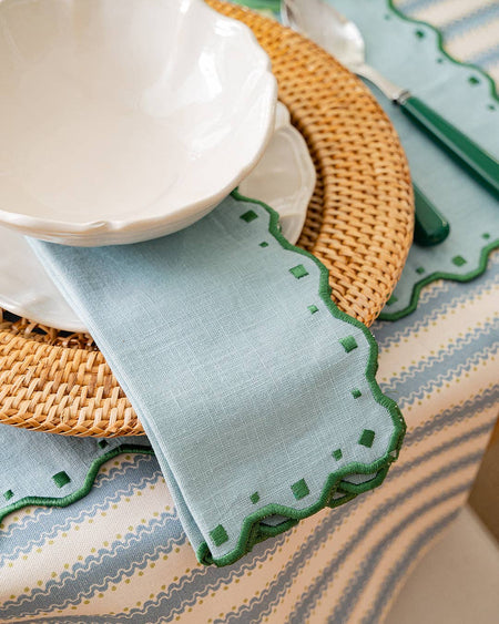 Light blue placemat with green scalloped edge on a patterned tablecloth