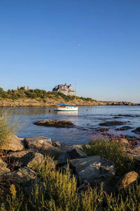 Coastal scene with a house on a hill overlooking a body of water with a boat.