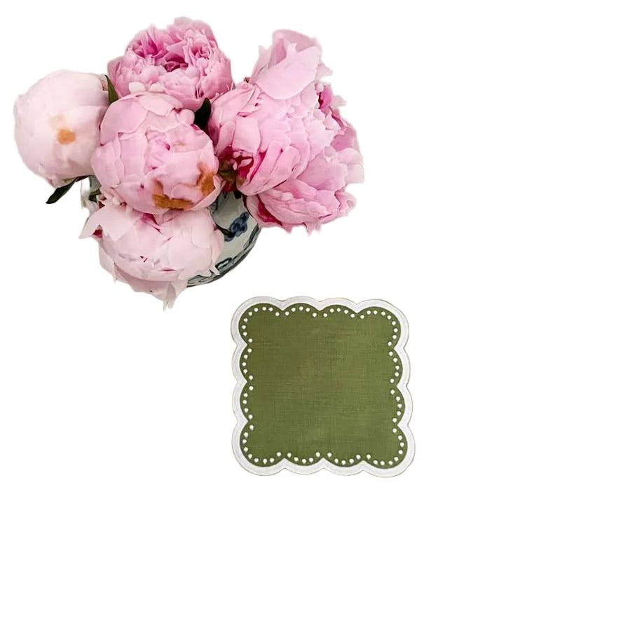 A scalloped cocktail napkin displayed next to a vase of pink flowers on a light background.