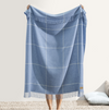 A person holding a sky blue windowpane cashmere throw with a classic checkered pattern and fringed edge detail.