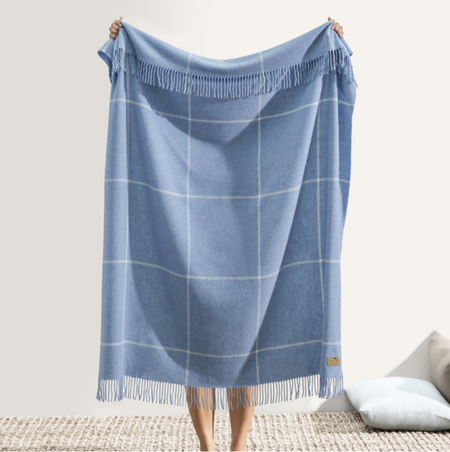 A person holding a sky blue windowpane cashmere throw with a classic checkered pattern and fringed edge detail.