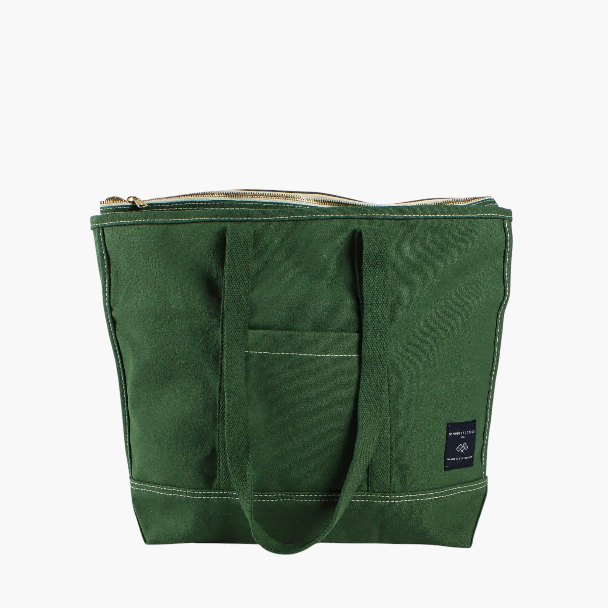 A dark green canvas tote bag with a top zipper, dual shoulder straps, a front pocket, and a small black brand patch on the lower right side, shown against a plain white background.