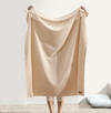 Beige throw blanket with fringes draped over a chair on a light background