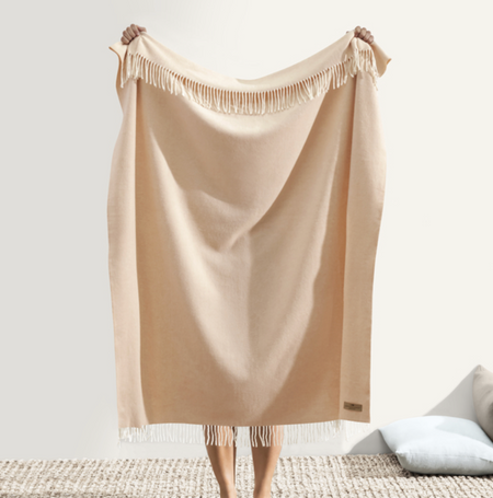 Beige throw blanket with fringes draped over a chair on a light background