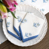 Set of white napkins with blue floral embroidery on a white plate with a wooden table background.