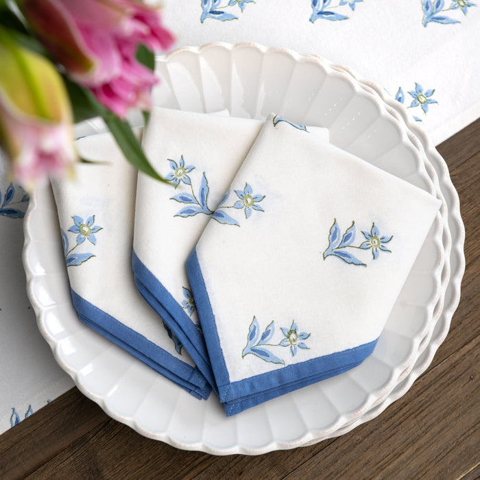 Set of white napkins with blue floral embroidery on a white plate with a wooden table background.