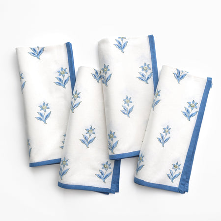 Set of four white napkins with blue floral embroidery on a white background