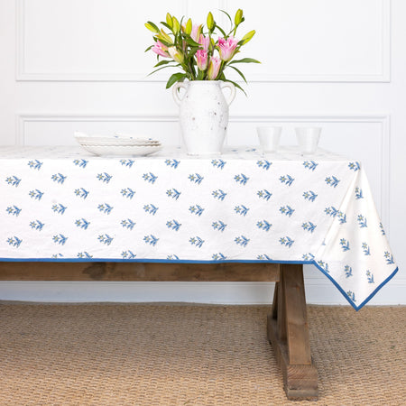 Tablecloth with blue floral pattern on a wooden table, with a vase of flowers in the background.