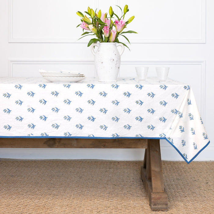 Tablecloth with blue floral pattern on a wooden table, with a vase of flowers in the background.