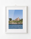 Framed photograph of a house by the water on a white wall