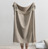 Beige blanket with fringe held by a person against a plain background