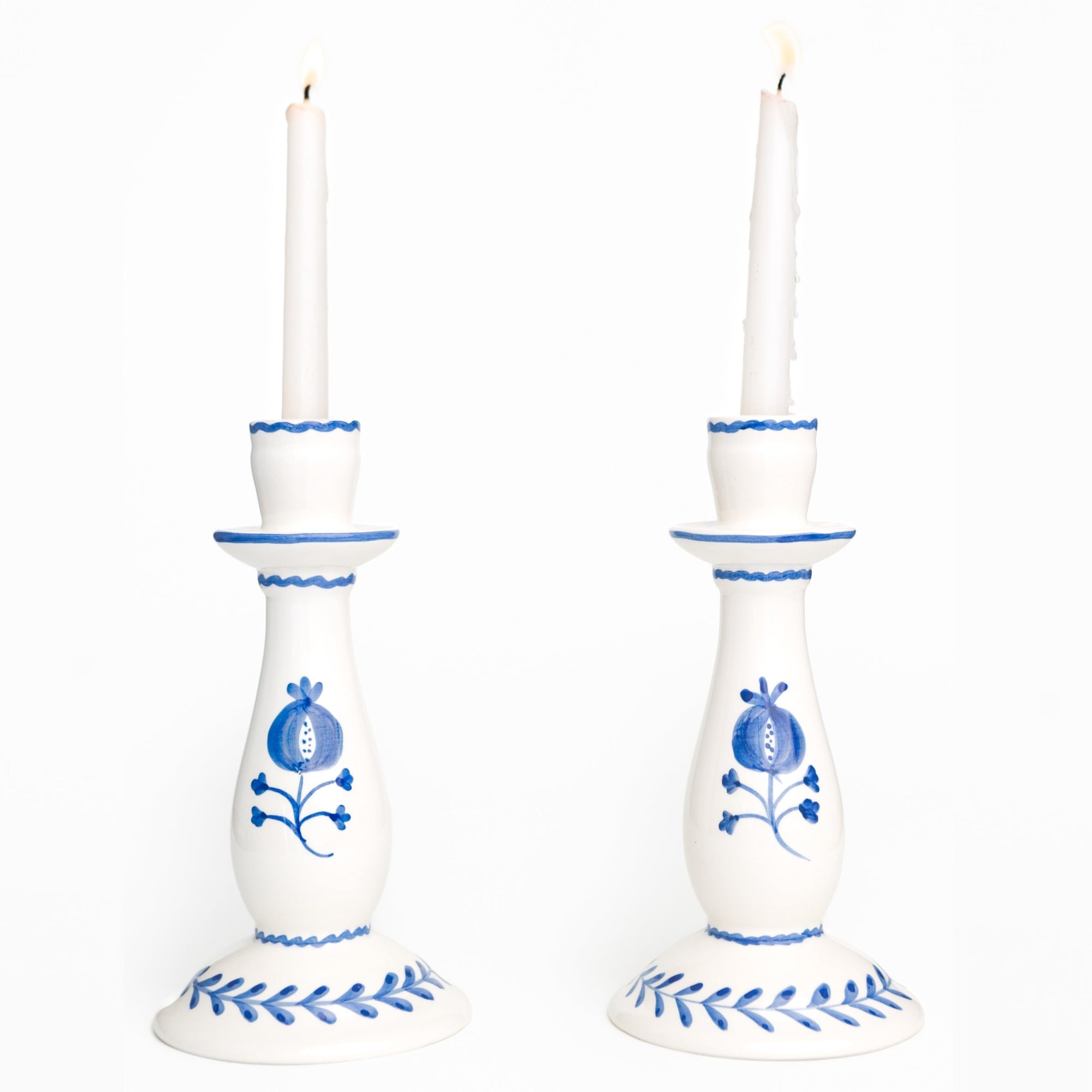 White candlesticks with blue floral patterns holding lit candles on a white background