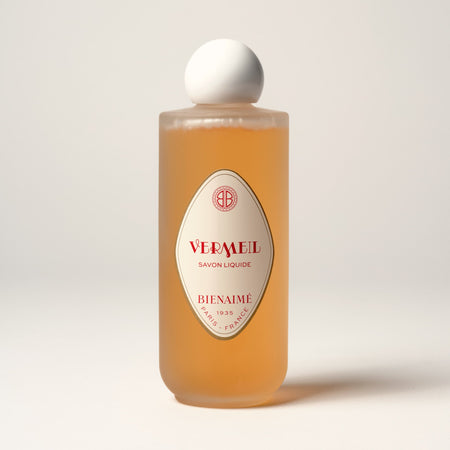 A clear bottle containing orange-colored liquid soap with a white cap, labeled 'Vermeil' and 'Bienaimé' with red and black text.