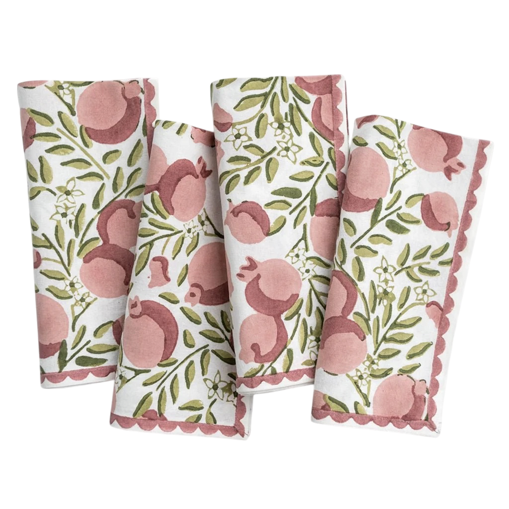 Four folded white napkins with a pink and green pomegranate pattern and scalloped edges, arranged on a white background.