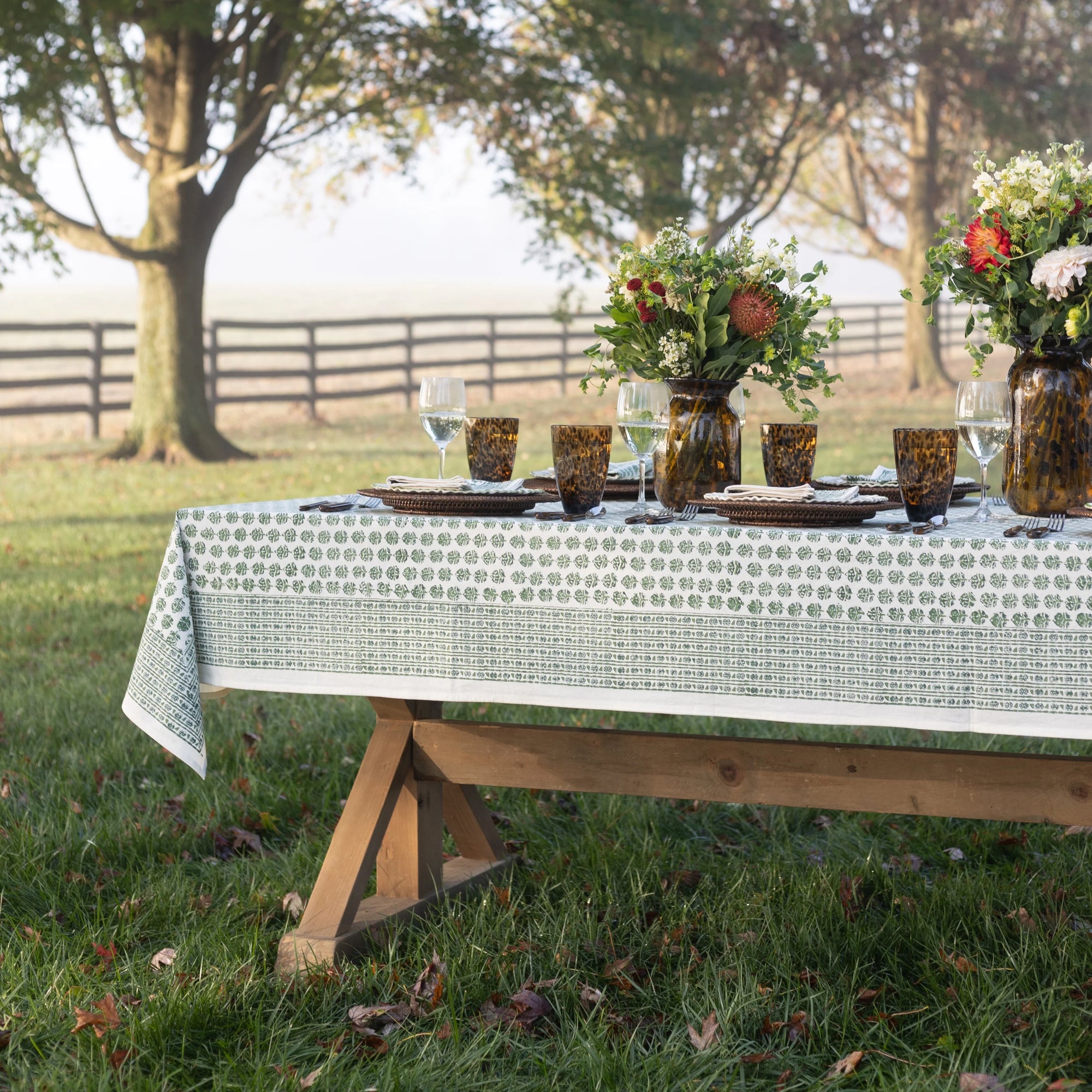 Set table outdoors with floral arrangements and a patterned tablecloth.