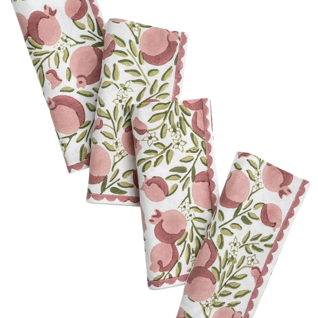 Three folded fabric napkins with a pomegranate and leaf pattern, arranged diagonally on a solid white background.