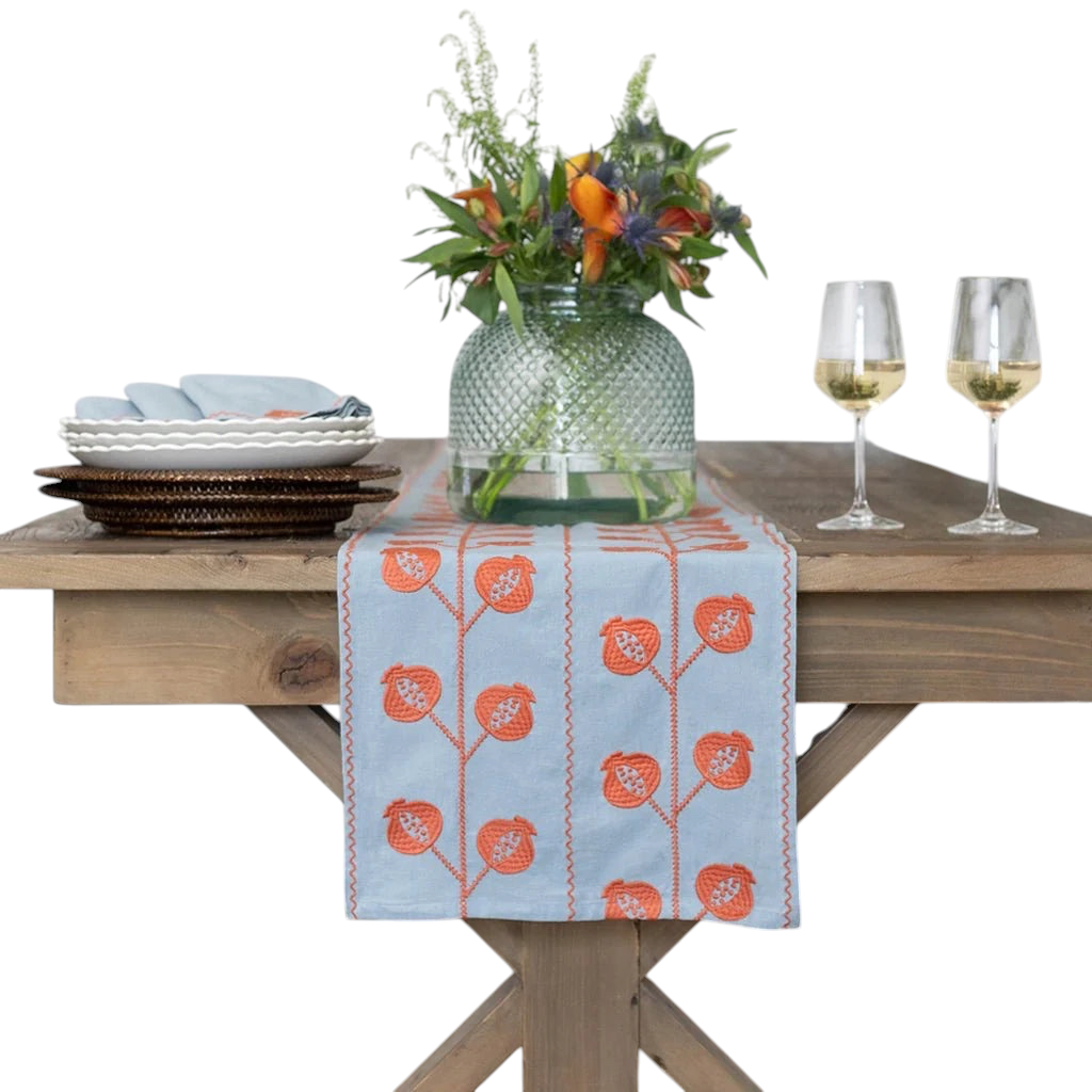 Homeport slate blue table runner with orange pomegranate crewel embroidery on a rustic wooden dining table