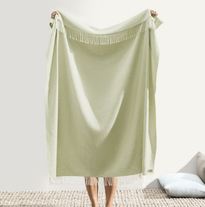 Light green blanket being held up on a white background