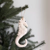 White seahorse ornament hanging on a Christmas tree branch.