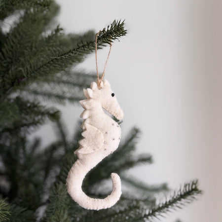 White seahorse ornament hanging on a Christmas tree branch.