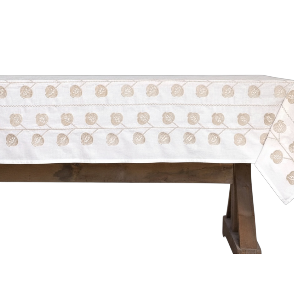 An off-white cotton tablecloth with a beige floral and vine pattern, draped over a rustic dark brown wooden bench against a solid white background.