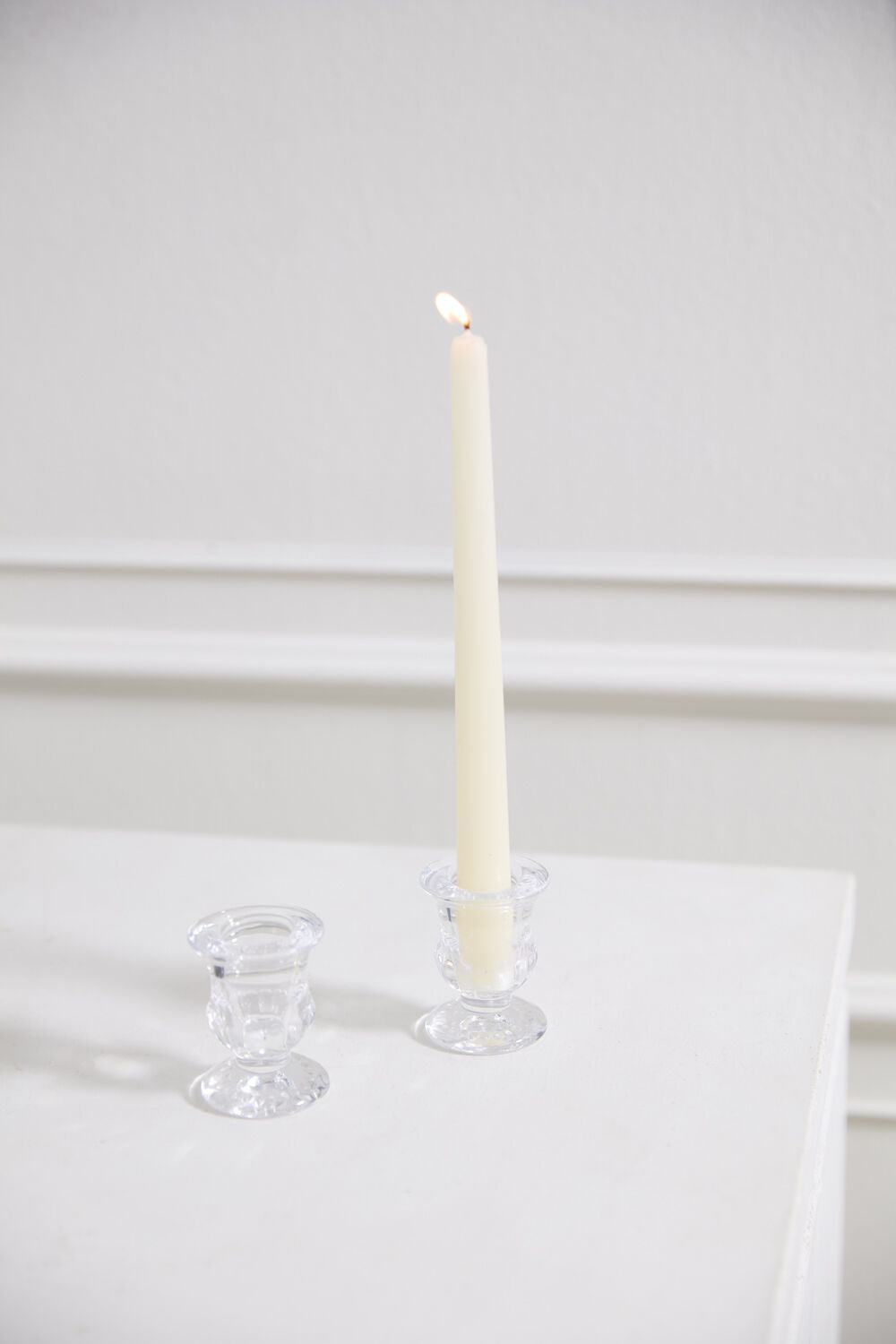 White candle in a glass holder on a white surface with a white background