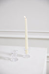 White candle in a glass holder on a white surface with a white background