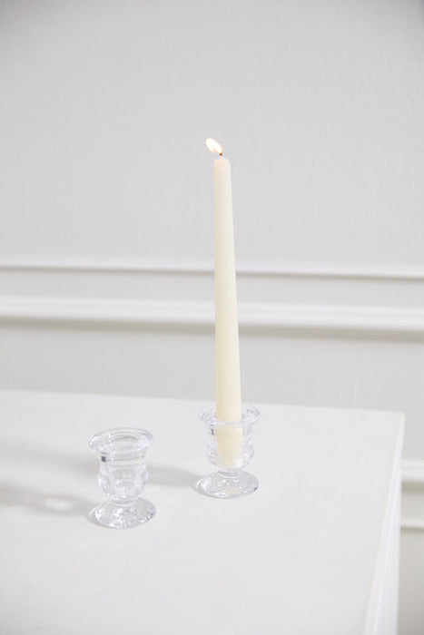 White candle in a glass holder on a white surface with a white background
