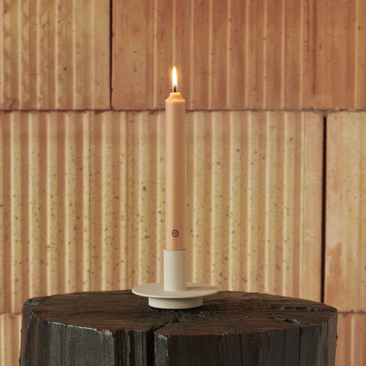 Candle in a white holder on a wooden stump with a wooden paneled background