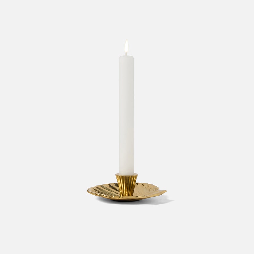 Gold candle holder with a white candle on a white background