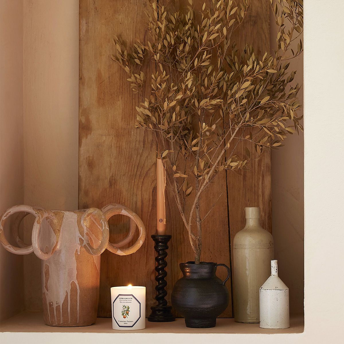 Decorative shelf with vases, a candle, and a plant against a wooden wall.