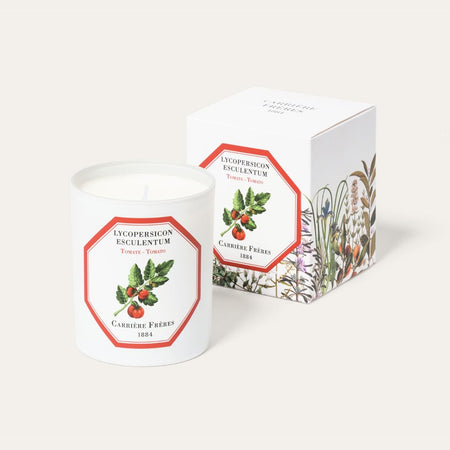A white candle with a red label featuring an illustration of a tomato, alongside its packaging box with a floral design.