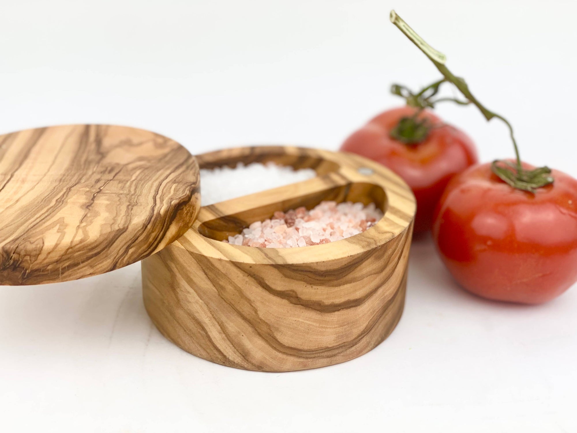 Wooden salt cellar with pink Himalayan salt and two tomatoes on a white background